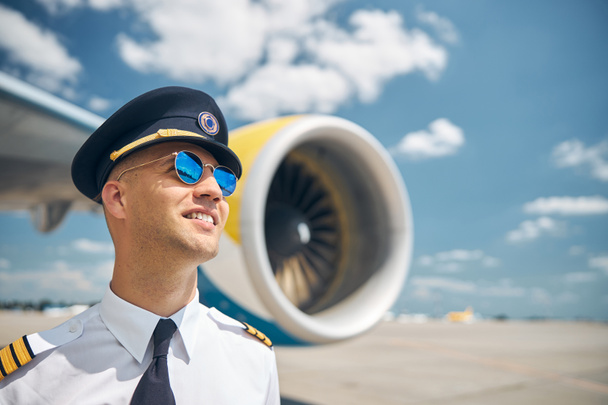 Alegre piloto masculino en gafas de sol de pie al aire libre en el campo de aviación - Foto, Imagen