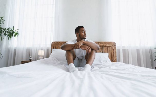 Thoughtful African American Man Looking Aside Sitting In Bedroom Indoors - 写真・画像