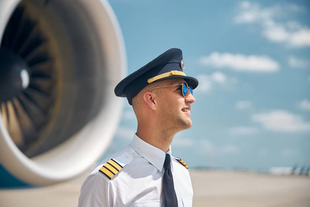 Piloto alegre en gafas de sol de pie al aire libre en el campo de aviación - Foto, Imagen