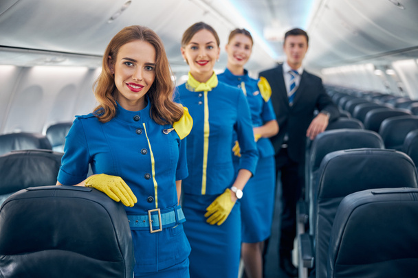 Happy cheerful aviation team in stylish blue and dark blue uniform standing in the salon of plane - Photo, Image