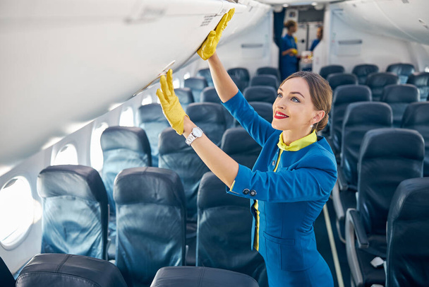 Belle hôtesse de l'air préparant et enregistrant compartiment avec bagages à main dans la cabine du passager - Photo, image