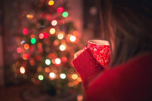 Young woman with cup of hot chocolate or tea or coffee in front of Christmas tree. Relaxing and christmas concept. - Foto, immagini