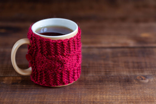 Cup of tea in red knitted cover on wooden texture - Fotó, kép