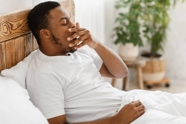Sonolento afro-americano cara bocejando acordar na cama interior - Foto, Imagem
