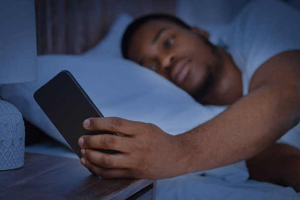 Ο τύπος διαβάζει το μήνυμα στο τηλέφωνο ξαπλωμένος στο κρεβάτι τη νύχτα - Φωτογραφία, εικόνα