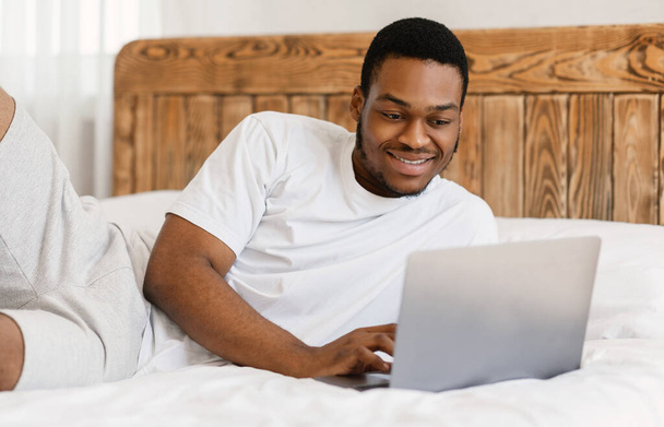 afroamericano freelancer hombre trabajando en portátil acostado en la cama - Foto, Imagen