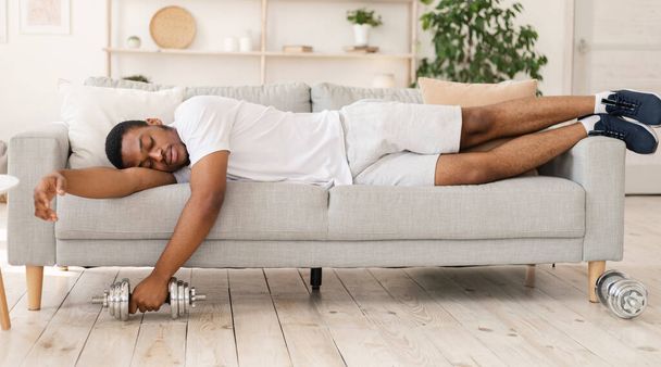 African American Man Sleeping Holding Dumbbell Lying On Couch Indoor - Zdjęcie, obraz