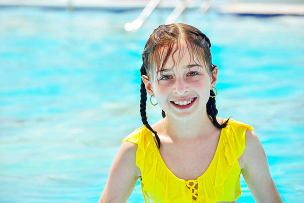 プールで泳いでいる女の子。プールで泳いでいると興奮した女の子が目を離す。楽しい子供時代だ。リラクゼーションの概念。10代だ。女の子笑いますでA黄色の水着でザ夏のプール. - 写真・画像