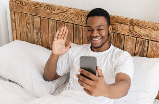 Africano chico haciendo videollamada en Smartphone acostado en la cama - Foto, imagen