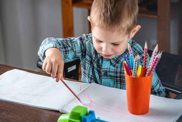 かわいい子供はテーブルのアルバムの紙に鉛筆で描いています。就学前教育の概念と創造性の発達 - 写真・画像