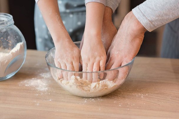 Gros plan des mains des hommes et des enfants pétrissant la pâte dans un bol - Photo, image