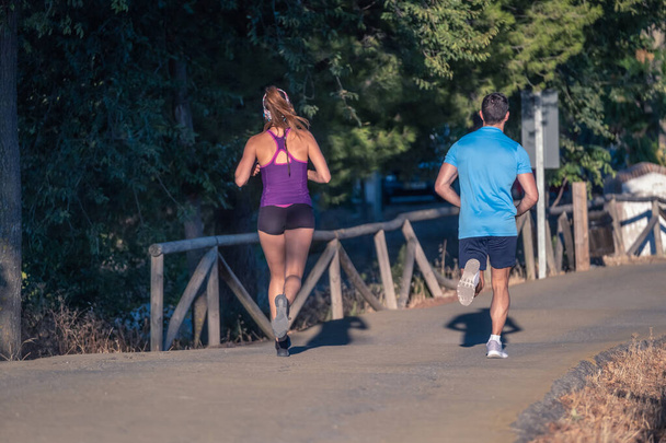 Молодий чоловік у блакитній футболці та молода жінка у фіолетовій футболці, що біжить у парку
 - Фото, зображення