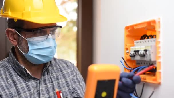 Electrician at work on an electrical panel protected by helmet, safety goggles and gloves; wear the surgical mask to prevent the spread of Coronavirus. Construction industry. Covid-19 Pandemic Prevention. Footage. - Footage, Video