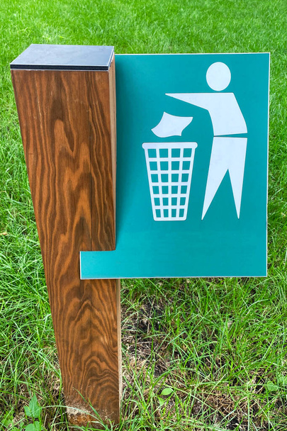 Sign of throw the trash in the trash can on background of green grass in park. Symbol on metallic plate. - Photo, Image