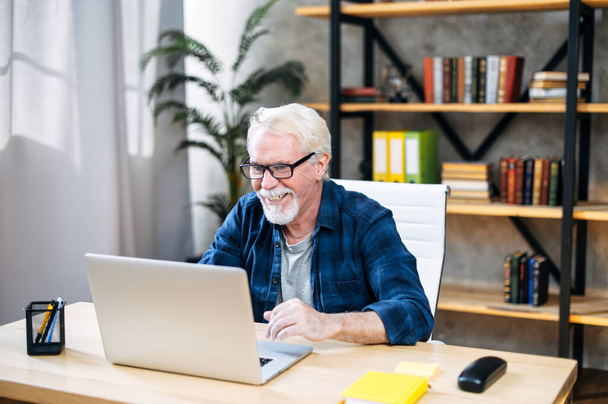 Older man is using laptop for working indoor - Фото, изображение