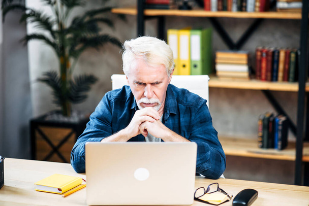 Older man is using laptop for working indoor - Fotó, kép