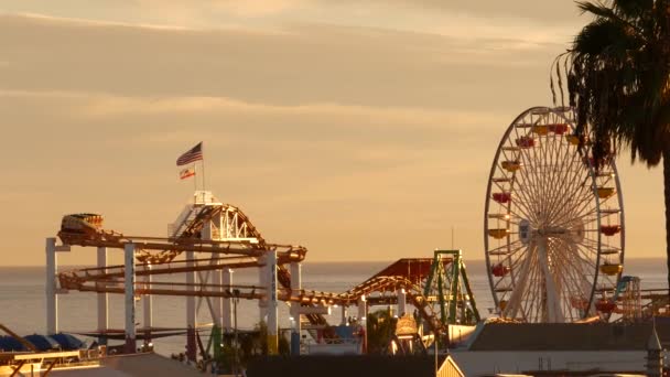 Klassinen maailmanpyörä, huvipuisto laiturilla Santa Monican meren rantalomakohteessa. Kesällä Kaliforniassa esteettinen, ikoninen näkymä, symboli Los Angeles, CA USA. Auringonlasku kultainen taivas ja nähtävyydet - Materiaali, video