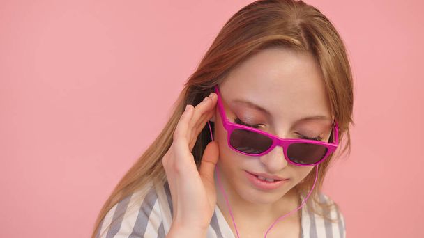 Young caucasian woman with sunglasses listening to the music using headphones . Isolated on pink background, close up - Photo, Image