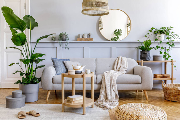 Stylish living room interior with design grey sofa, coffe table, rattan pouf, basket, shelf, mirror, tropical plants, decoration, carpet and elegant personal accessories in modern home decor. - Photo, Image