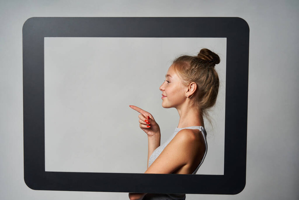 Profile of girl standing behind digital tablet frame and pointing a finger at blank copy space - Photo, image