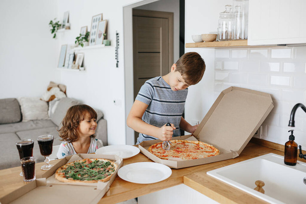 Happy time of eating concept. Kids boy and girl eating pizza at home. Two Adorable children enjoy eating pizza with a very happy emotional expressions of faces and postures. - Фото, изображение