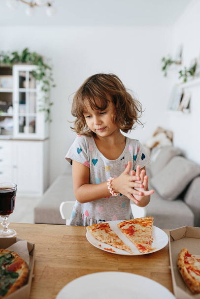 Happy time of eating concept. Kids girl eating pizza at home. Adorable childr enjoy eating pizza with a very happy emotional expressions of face - Foto, imagen