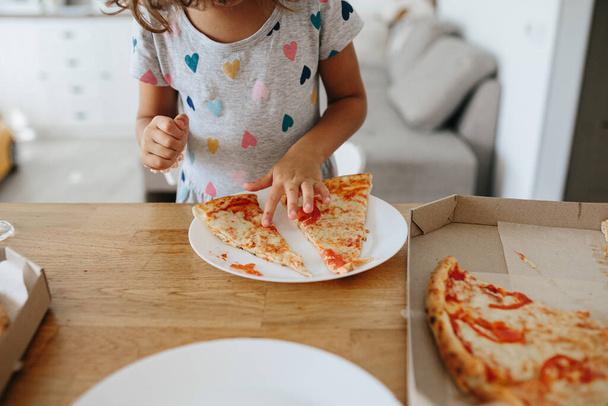 Happy time of eating concept. Kids girl eating pizza at home. Adorable childr enjoy eating pizza with a very happy emotional expressions of face - Фото, зображення
