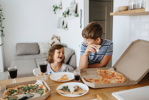 Happy time of eating concept. Kids boy and girl eating pizza at home. Two Adorable children enjoy eating pizza with a very happy emotional expressions of faces and postures. - Foto, Imagem