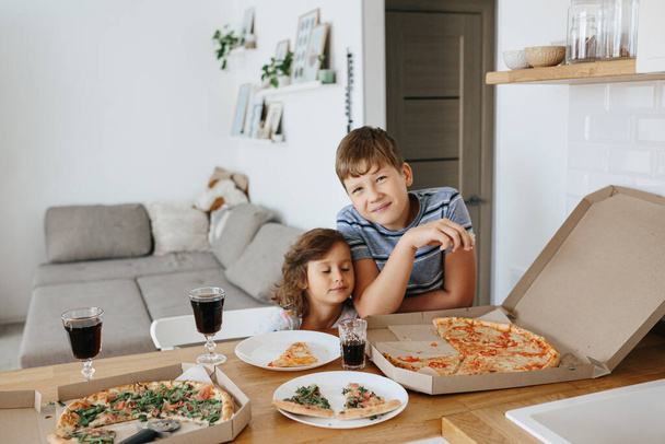Happy time of eating concept. Kids boy and girl eating pizza at home. Two Adorable children enjoy eating pizza with a very happy emotional expressions of faces and postures. - Fotoğraf, Görsel