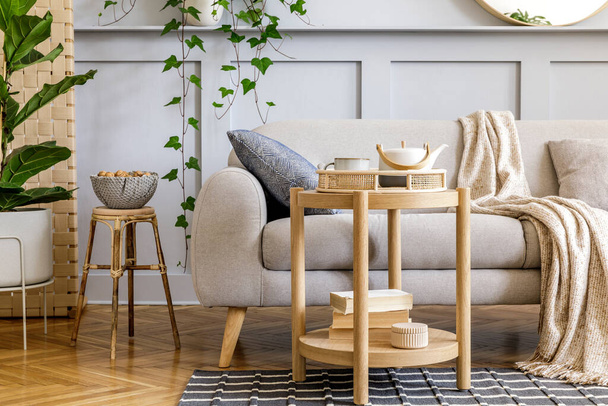Scandinavian living room interior with design grey sofa, wooden coffee table, tropical plants, shelf, mirror, furniture, plaid pillow, teapot, book and elegant personal accessories in home decor. - Φωτογραφία, εικόνα
