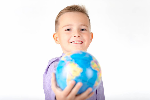 Close up jovem caucasiano escola menino mostra na frente de um globo no fundo estúdio branco. - Foto, Imagem
