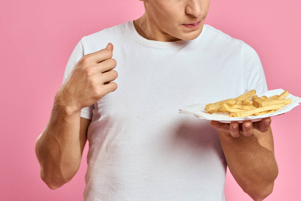 Férfi sült krumplival egy papírdobozban egy rózsaszín háttér kalória gyorsétterem portré rózsaszín háttér - Fotó, kép