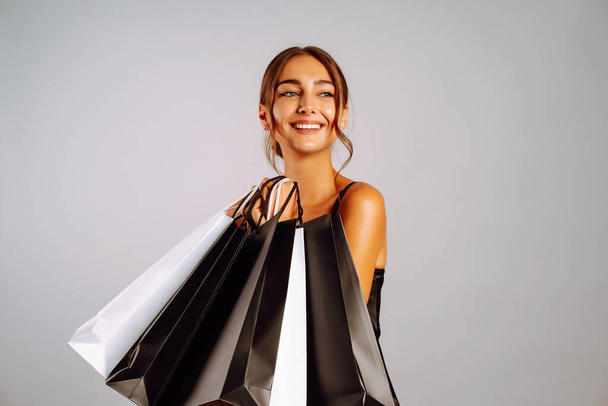 Elegant brunette woman in black dresse holding shopping bags. Young woman with black and white bags posing on grey background. Purchases, black friday, discounts, sale concept. - Фото, зображення