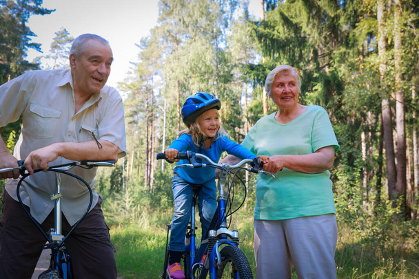 ενεργό ζευγάρι ηλικιωμένων με μικρή εγγονή σε ποδήλατα στη φύση - Φωτογραφία, εικόνα