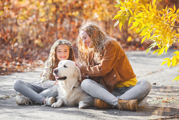 Kaksi söpöä tyttöä kävelemässä lemmikkinsä kanssa. Siskot ja koira syksyllä taustalla - Valokuva, kuva
