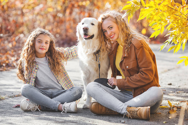 Dos chicas lindas caminando con su mascota. Hermanas y perro en el fondo de otoño - Foto, imagen