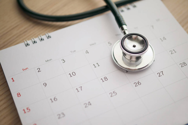 Stethoscope με ημερομηνία ημερολογιακή σελίδα στο ξύλινο τραπέζι φόντο γιατρό ραντεβού ιατρική έννοια - Φωτογραφία, εικόνα