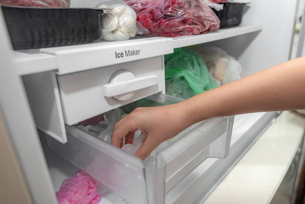 La chica toma hielo de la máquina de hielo del congelador para refrescar las bebidas. - Foto, Imagen