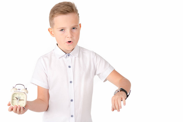 Surprised schoolboy with alarm clock and wach, isolated on white wall. - Foto, Bild