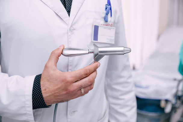La main du médecin tient l'instrument pour le traitement des hémorroïdes dans le contexte d'instruments médicaux flous dans la salle d'opération - Photo, image