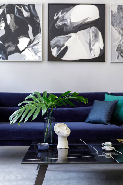 Stylish and modern living room interior with blue velvet sofa, mock up paintings, design furniture, plant, table, decoration, concrete floor, elegant personal accessories in home decor. - Foto, afbeelding