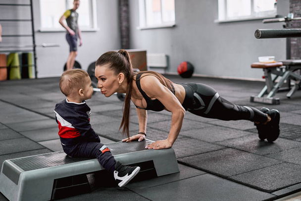 Young fit woman doing push-ups and kissing her little son - Foto, afbeelding