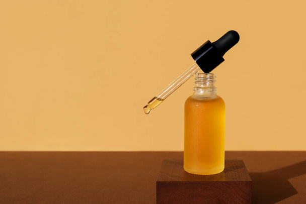 Mockup of cosmetic oil bottle with dropper removed on wooden stand. Horizontal monochrome brown banner, copy space. Natural lotion, essence, serum, emulsion. Frosted amber vial, black cap, front view - Фото, изображение