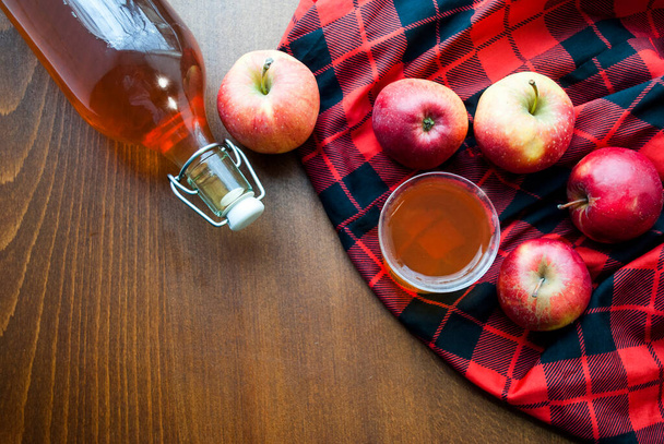 Bir şişe ve bardağın üst görüntüsü ev yapımı elma suyu. Siyah-kırmızı kareli masa örtüsü olan ahşap bir masanın üzerinde.. - Fotoğraf, Görsel