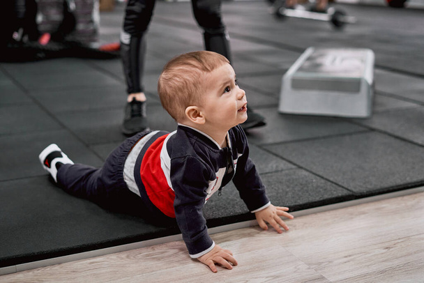 Little kid crawling on the floor while his mother doing exercises - Fotoğraf, Görsel