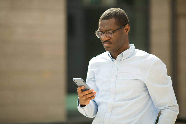 handsome young african man in shirt wearing glasses with phone in hand - Photo, Image