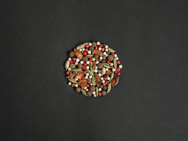 Vários temperos secos - anis de estrela, cardamomo, pimenta da Jamaica, pimenta rosa e branca reunidos em um modelo na forma de um círculo no fundo preto. Vista superior. Espaço de cópia - Foto, Imagem