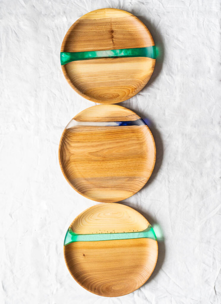 Vari vassoi artigianali rotondi in legno con inserti in resina su fondo tessile bianco. Vista dall'alto. Copia spazio - Foto, immagini