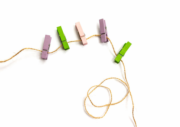 Des pinces à linge en bois multicolores reposent sur une corde isolée sur fond blanc vue d'en haut - Photo, image