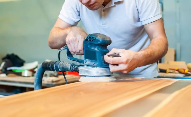 O homem trabalha com um moedor eléctrico. Artesanato de uma mesa de madeira em uma oficina de carpintaria. Close-up - Foto, Imagem